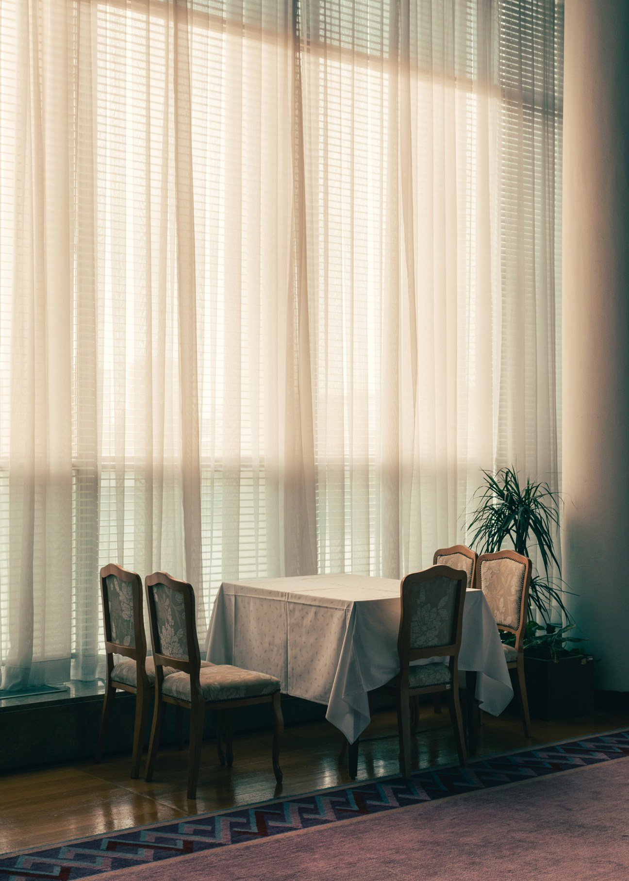 Mid-century modern lounge area with wooden chairs and small table beside floor-to-ceiling sheer curtains in the Croatian salon.