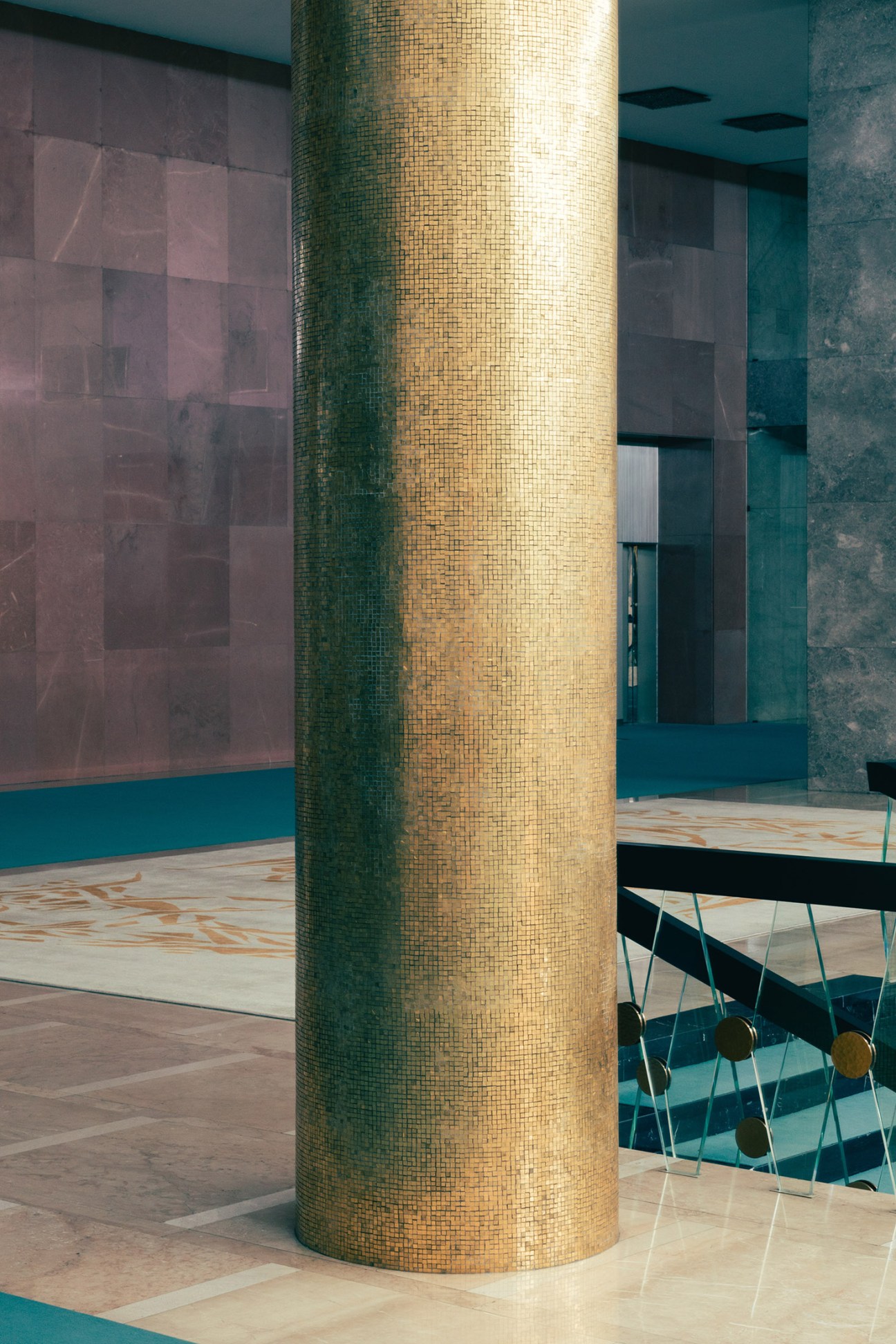 Gold mosaic pillar in the Hall of Yugoslavia at the Palace of Serbia with teal walls and mid-century modern furnishings.