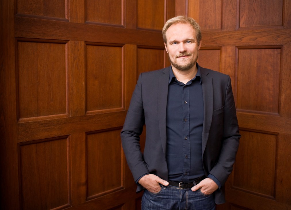 Rolf Hay, founder of Hay, stands against a wooden panelled wall wearing a dark blazer and shirt.