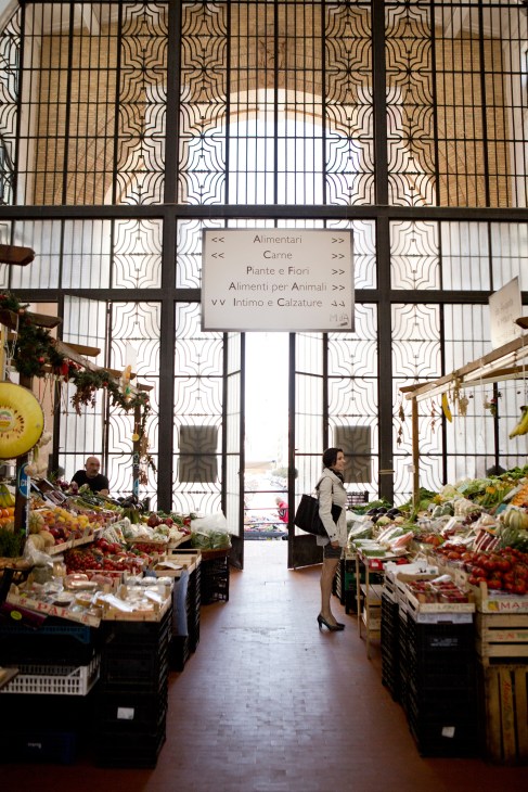 Interior of covered market in Rome's Trieste neighbourhood with ornate metal gates, produce displays, and shoppers browsing vegetables and fruits.
