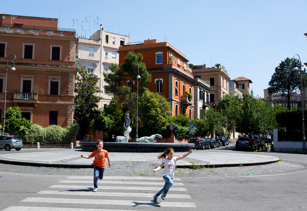 Children playing in a sunny Roman square surrounded by terracotta-colored buildings.