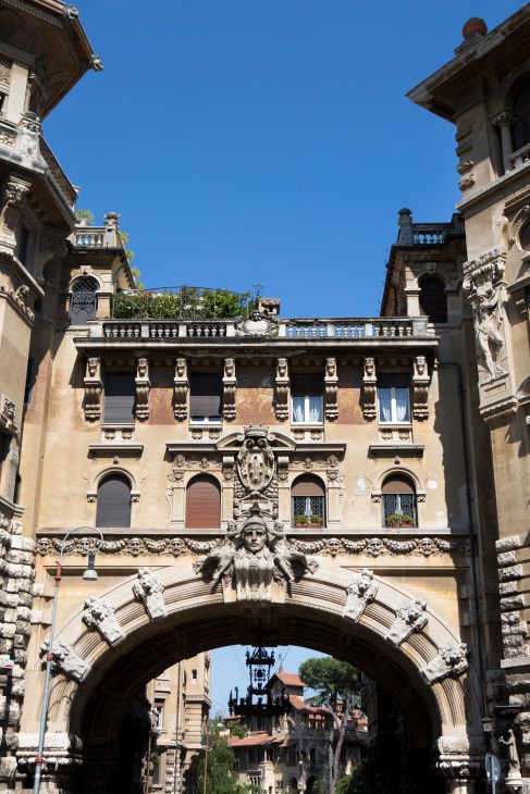Ornate archway with sculptural head and decorative stone carvings connecting two Renaissance buildings in Quartiere Coppedè, Rome.