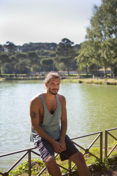 Man sitting on railing by a lake with forested hills in background