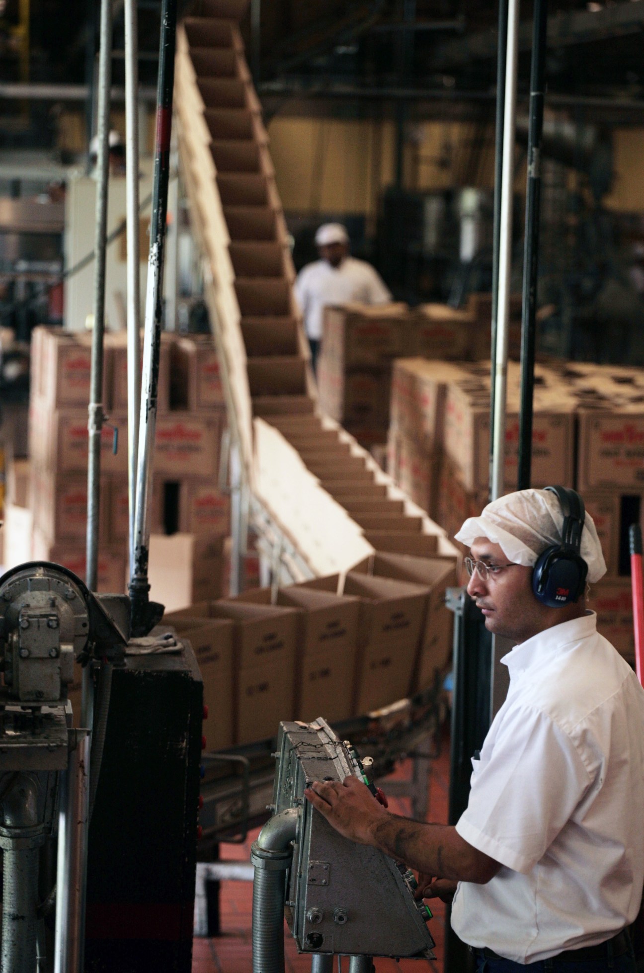 Worker in white shirt and headwrap operating machinery in a rum distillery facility.