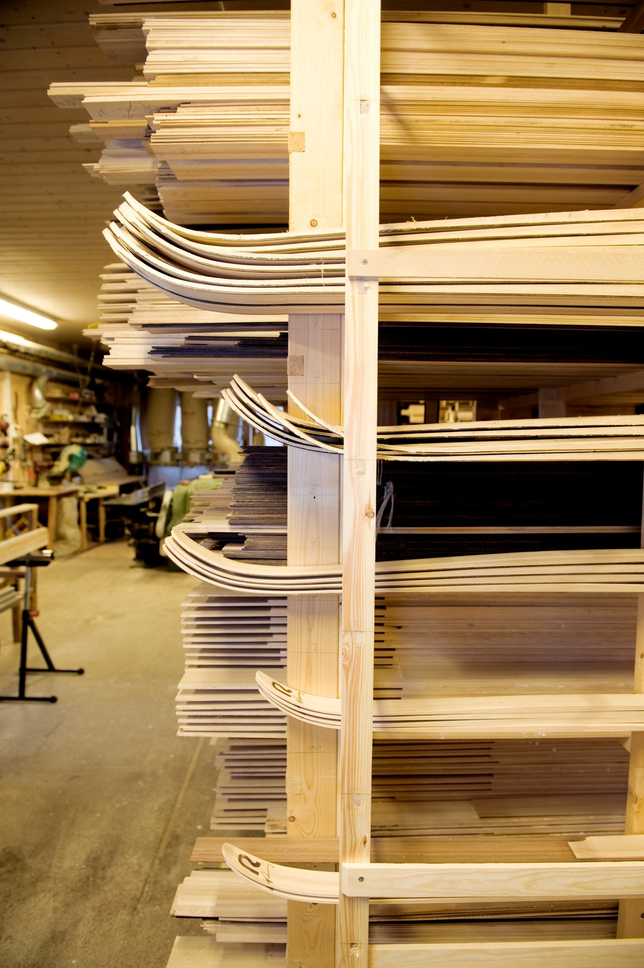 Wooden skis stacked on shelves in a factory workshop awaiting oil treatment.