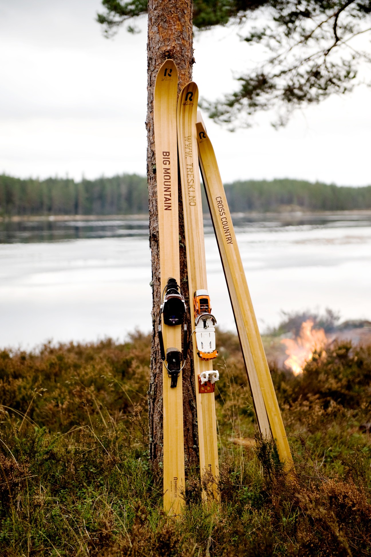 Wooden Rønning skis leaning against a tree by a Norwegian lake and forest landscape.