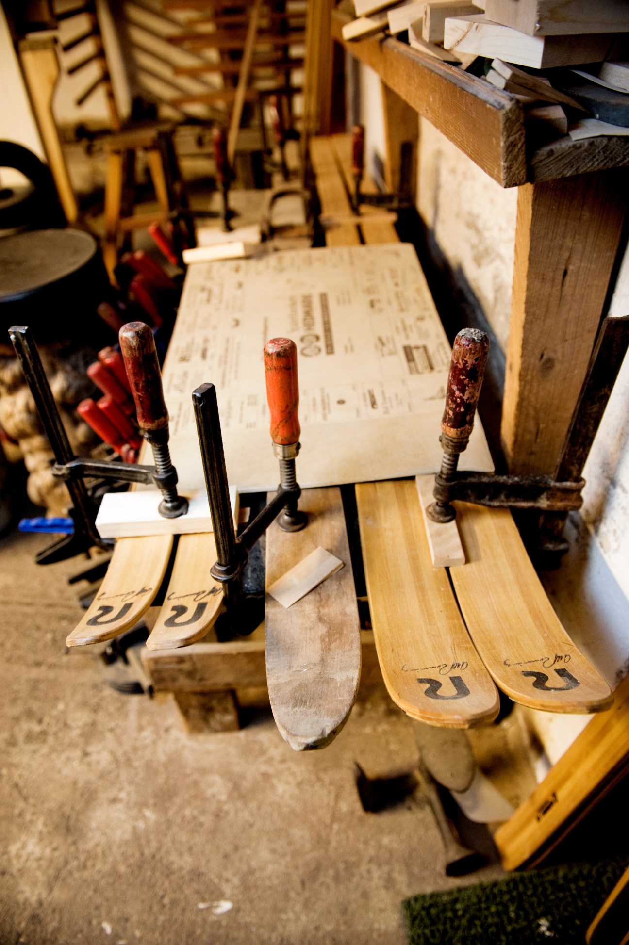 Wooden skis in a vice with wooden handles marked with the Rønning Ski logotype during handcrafting.