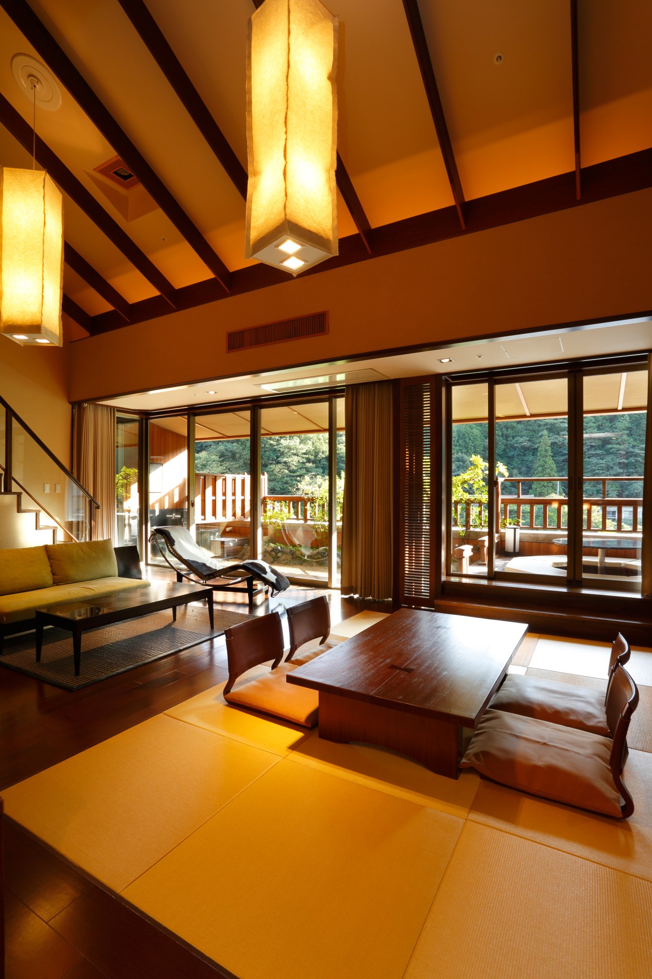 Modern ryokan suite with warm lighting, wooden beams, tatami mat flooring, and floor-to-ceiling windows overlooking mountains at Bettei Otozure.