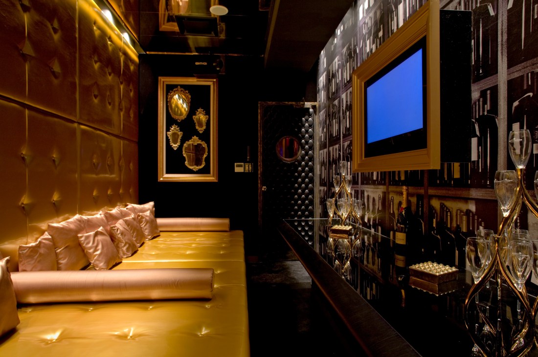 Luxurious karaoke room with gold vinyl daybed, padded walls, framed artwork, and plasma screen for karaoke.