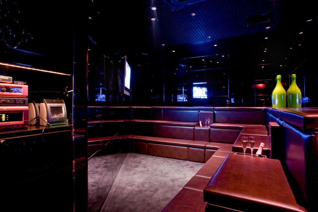 Marc Newson-designed karaoke room with tiered brown leather seating, carpeted performance space, and blue and red ambient lighting.