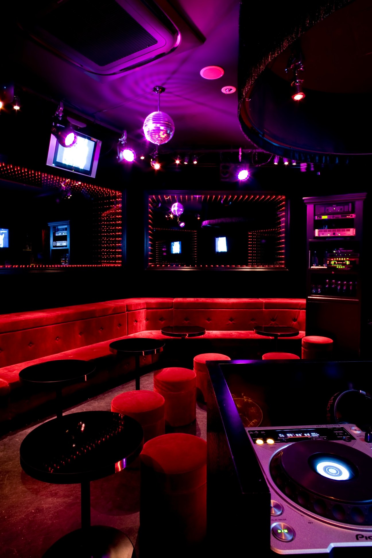 Amour karaoke room with red velvet seating, disco ball, neon-lit mirrors, DJ equipment and purple ambient lighting.
