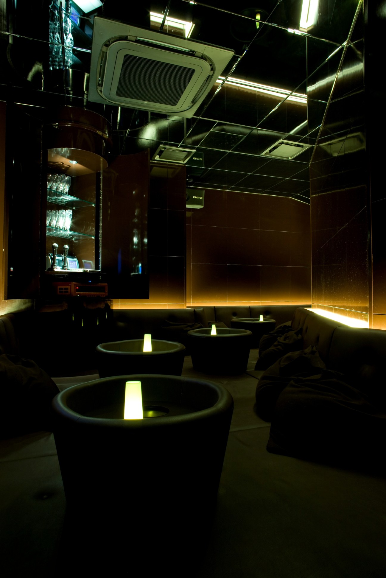 Room D at Amour karaoke venue with black leather platform, circular illuminated tables, and mirrored walls and ceiling.