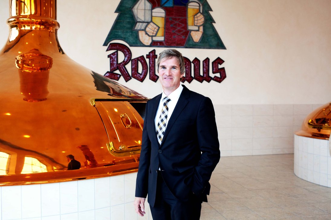 Christian Rasch, CEO of Rothaus brewery, standing in front of copper brewing kettles and the Rothaus logo.