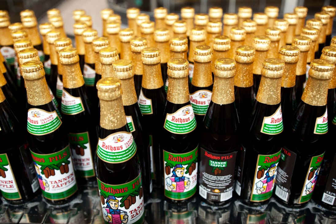 Multiple bottles of Rothaus beer with gold foil caps and colorful labels arranged in rows.