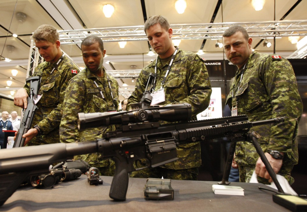 Military personnel in camouflage uniforms examining rifles and firearms at an indoor exhibition.