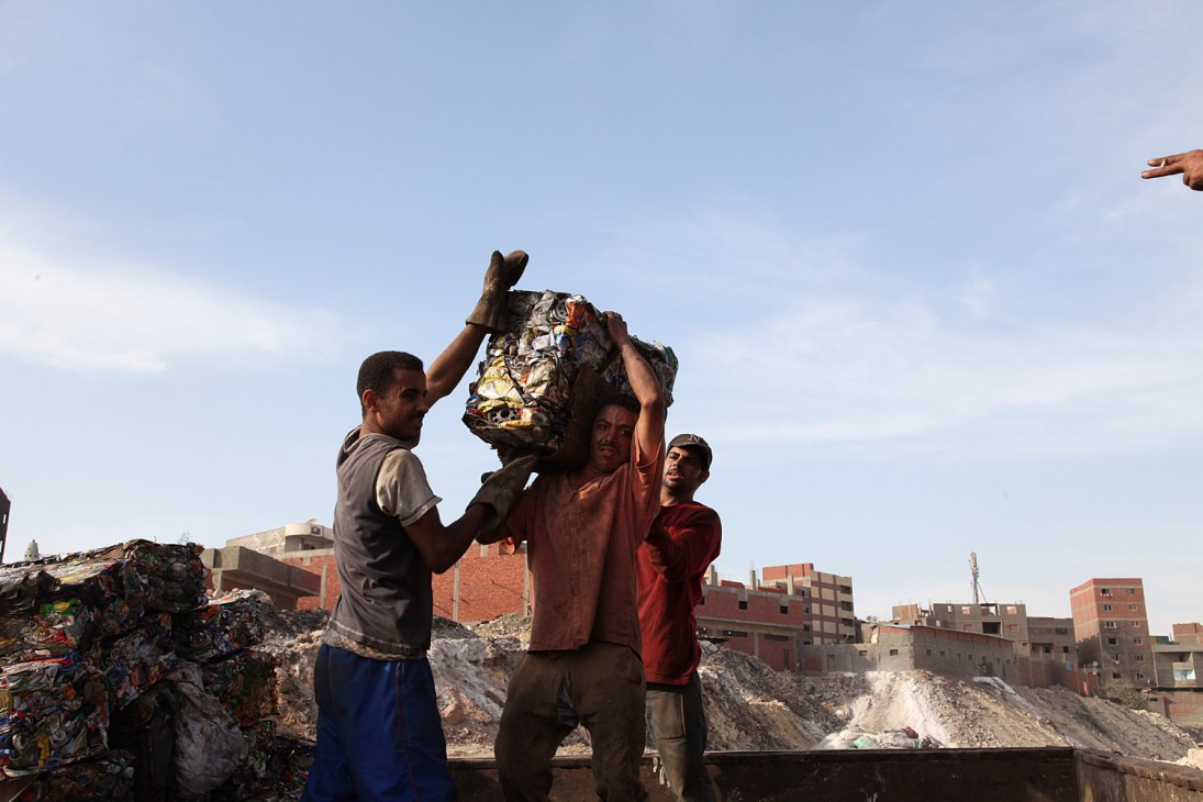 Workers handle waste at a Cairo rubbish dump with apartment buildings visible in the background.