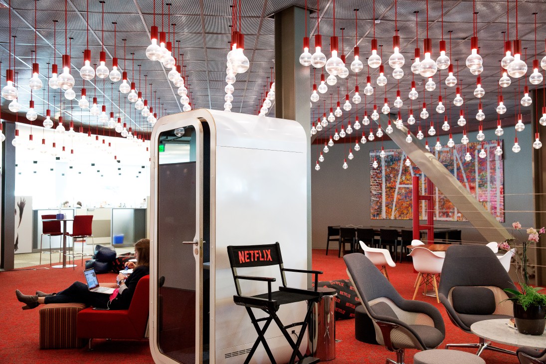 Netflix office communal workspace with red carpet, modern furniture, hanging pendant lights, and a white pod structure.