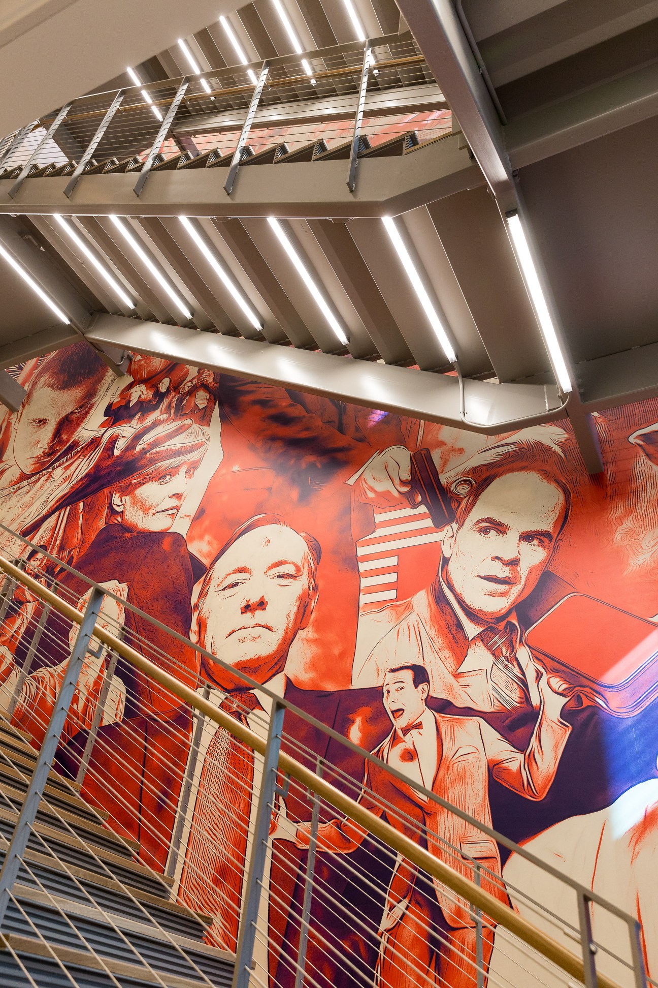 Modern stairway with linear ceiling lights and large red-toned portrait mural on wall below.