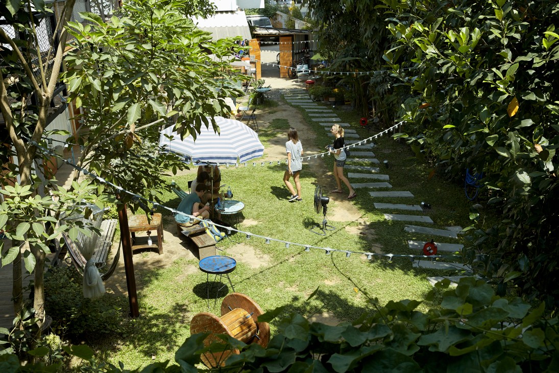 Travelers relax in the lush garden of The Yard hostel in Bangkok's Ari neighborhood