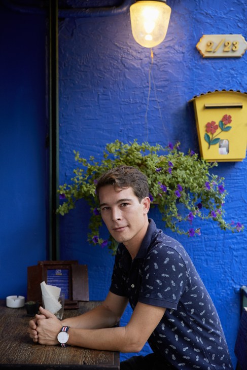 Man sitting at table against bright blue wall with yellow mailbox and hanging light fixture