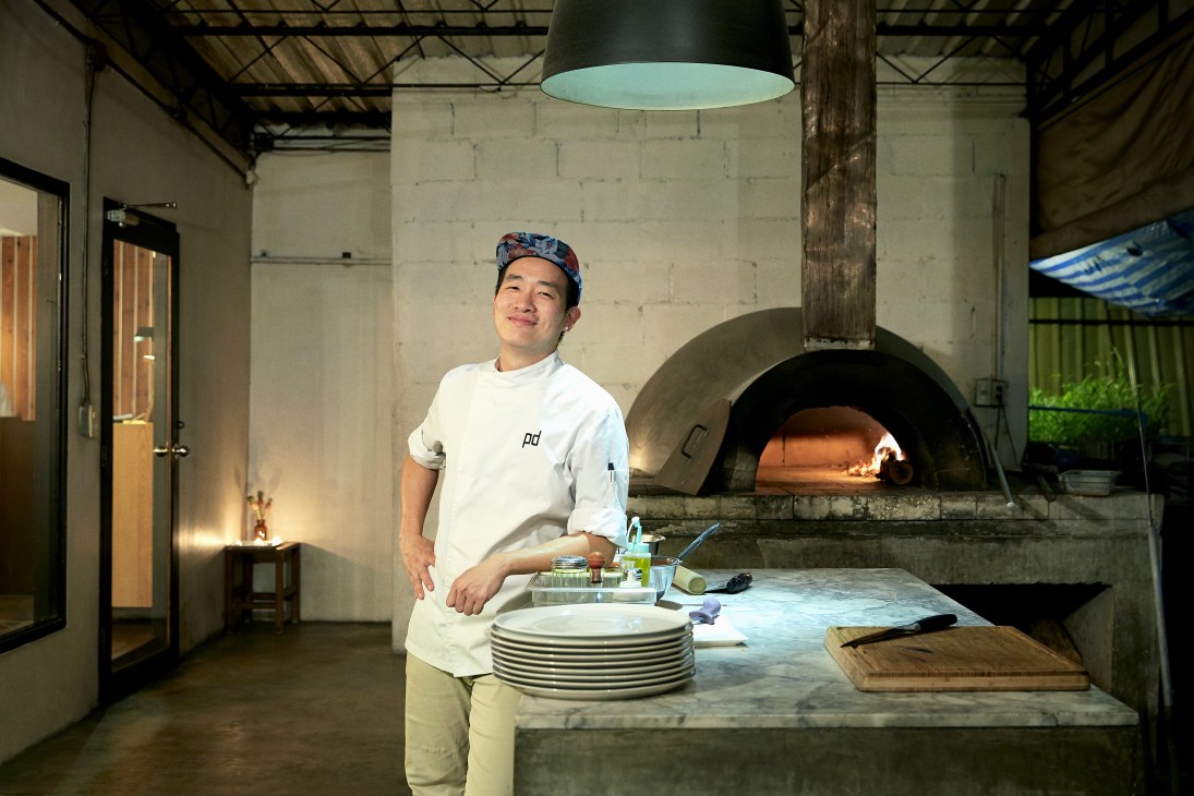 Chef Nattawut Traisinsathit standing in a modern restaurant kitchen with a wood-fired oven at Pla Dib