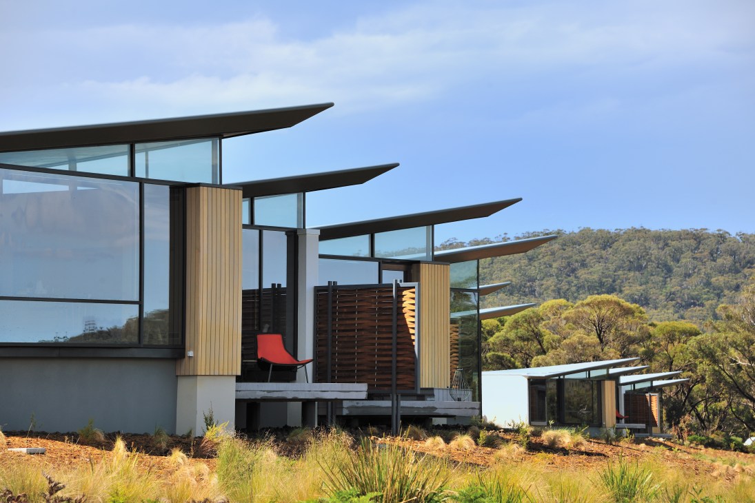 Modern Saffire Hotel with curved black roof overhangs, wooden cladding, and floor-to-ceiling windows overlooking forested landscape in Tasmania.