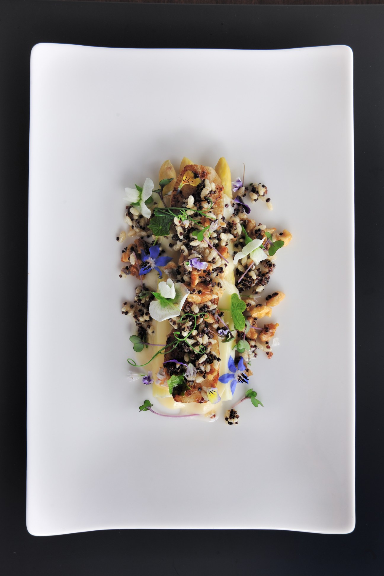 Plated dish with grains, edible flowers, and microgreens on white plate.