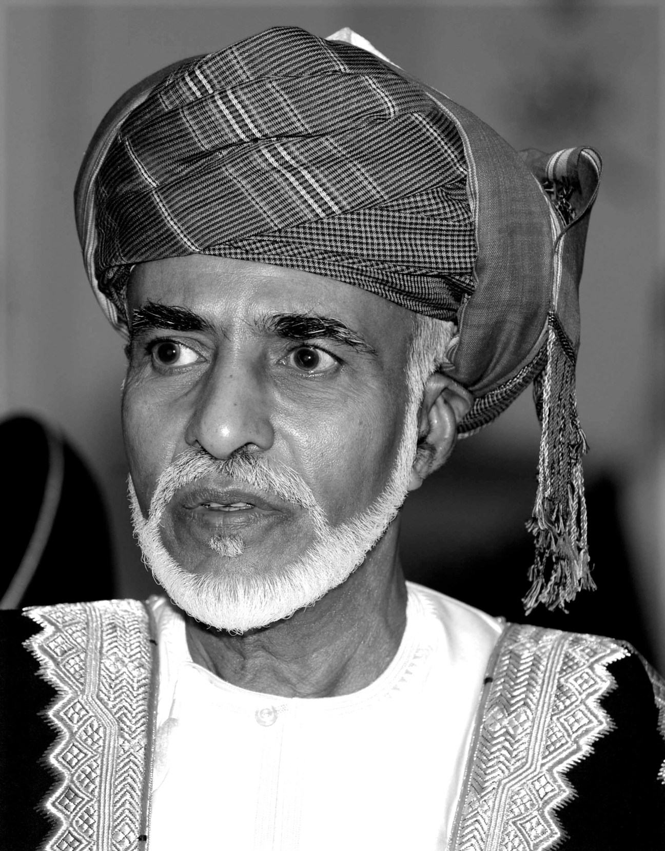 Black and white portrait of Sultan Qaboos wearing traditional Omani headwear and embroidered robe.