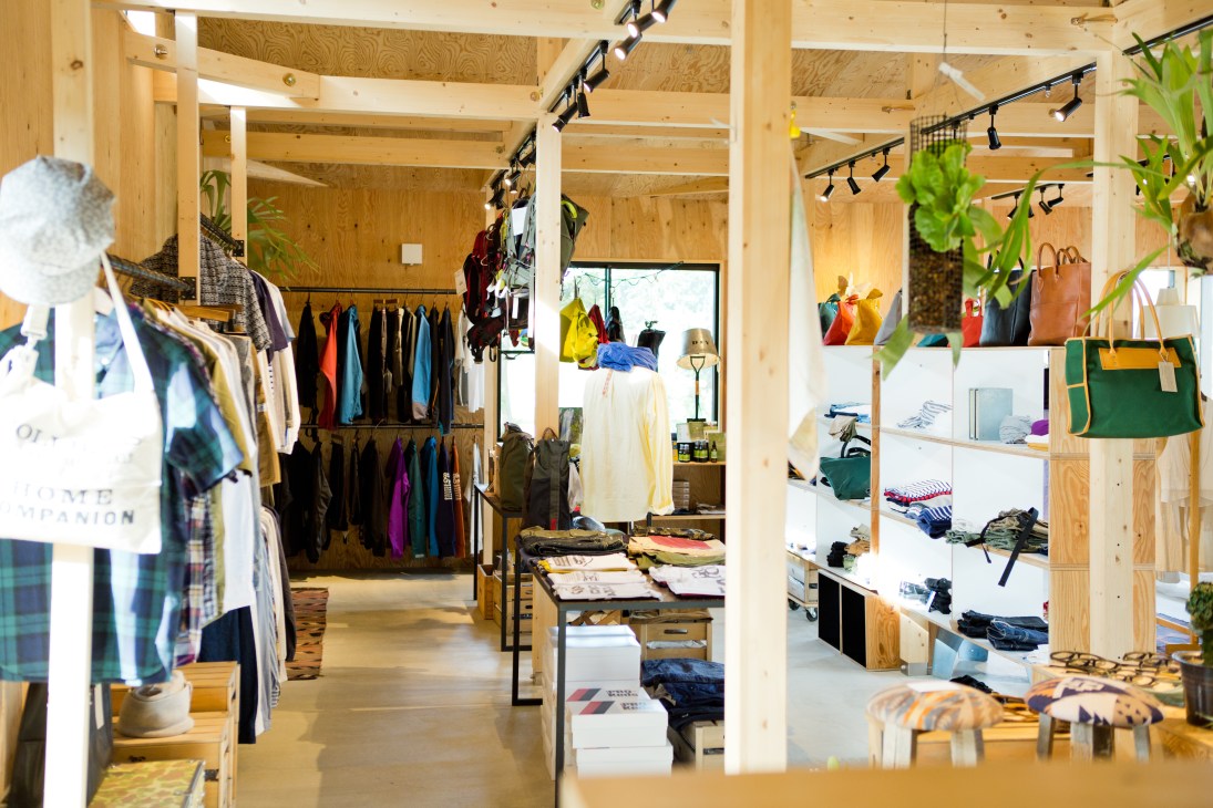 Interior of Salt shop in Hokkaido featuring wooden beams, clothing racks, white shelving, potted plants and natural lighting.