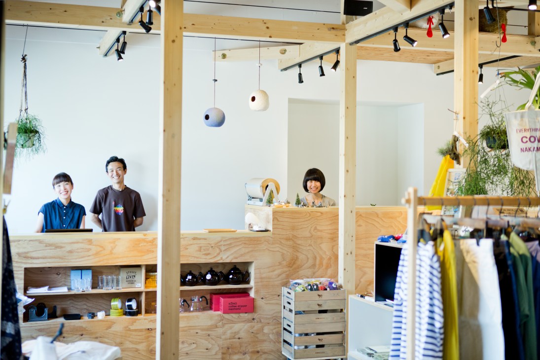 Salt owners Tomomi and Katsunori Yoneyama stand behind wooden counters in their minimalist shop interior with pendant lights and potted plants.
