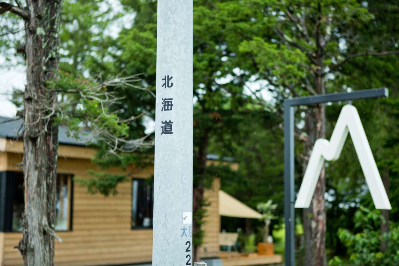 Salt's shop sign featuring Japanese characters on a white pole with wooden buildings and trees in background