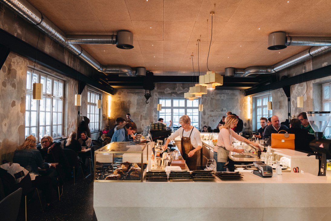 Busy coffee shop interior with baristas working behind counter and customers seated at tables