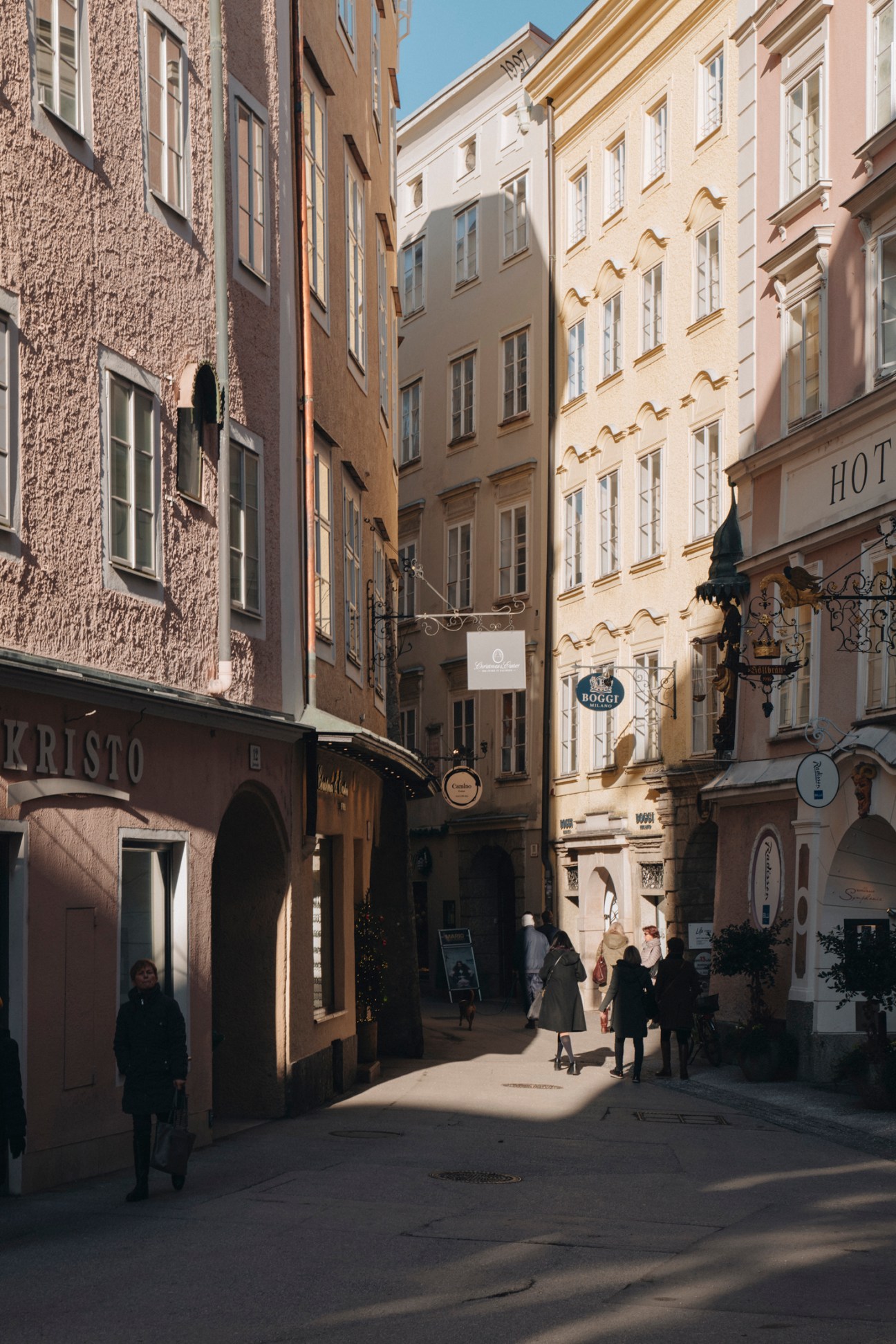 Narrow cobblestone street in Salzburg's old town with baroque buildings, traditional shop signs, and pedestrians walking