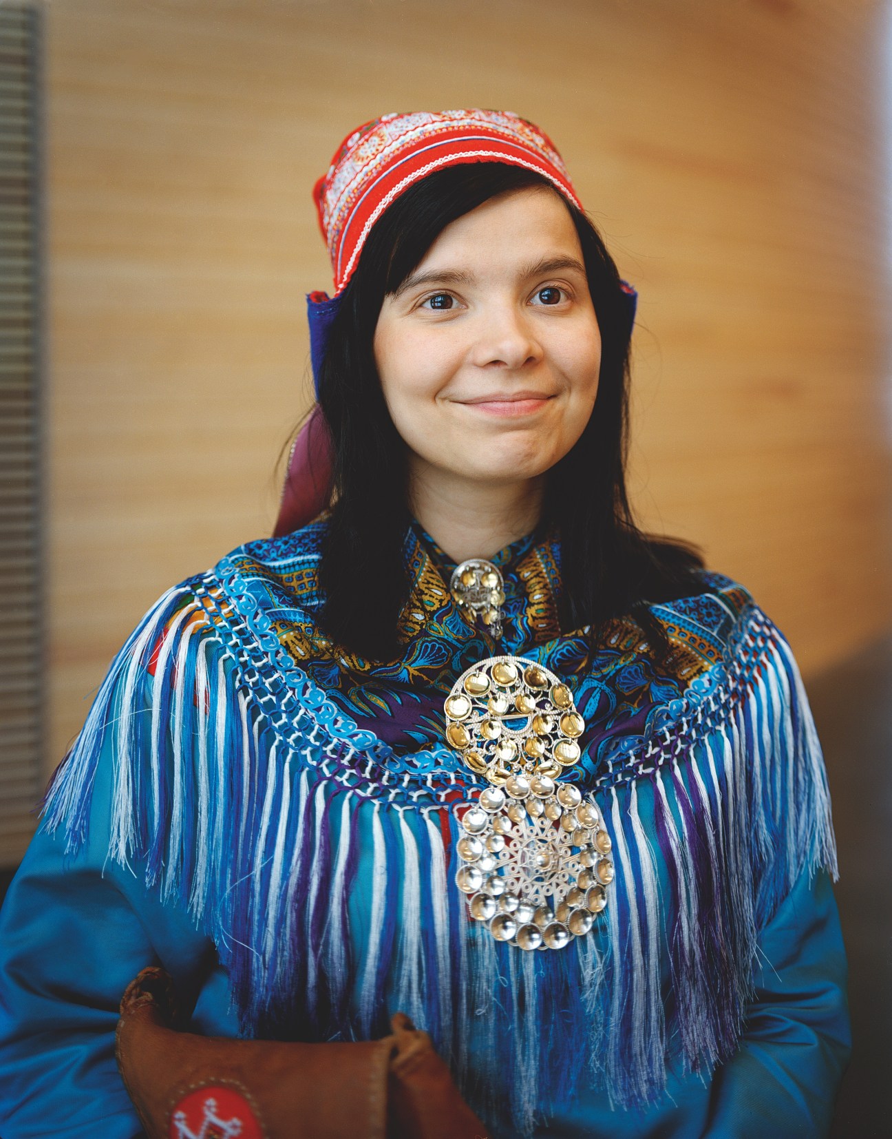 Rauni Äärela wearing traditional Sámi gákti dress with red beaded bonnet and silver solju brooch ornaments.