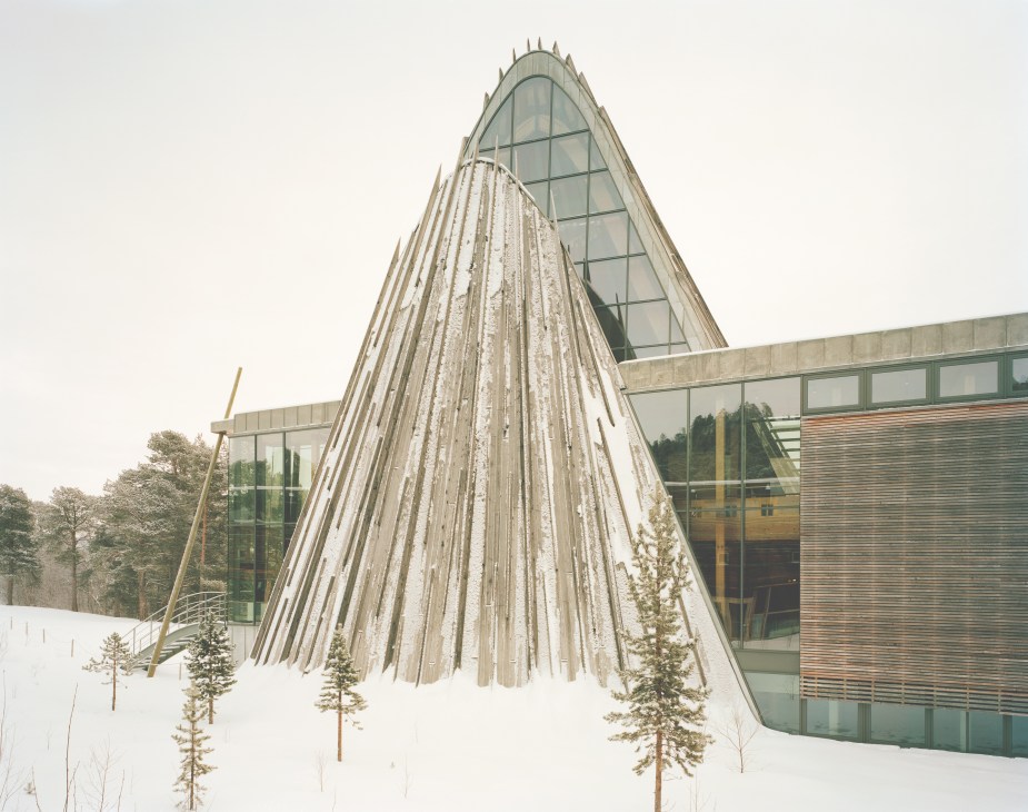 Norwegian Sámi Parliament building with tipi-inspired wooden structure and glass sections in snowy landscape.