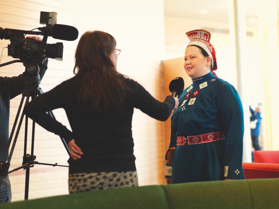 Tiina Sanila-Aikio in traditional Sámi dress being interviewed by a camera operator.