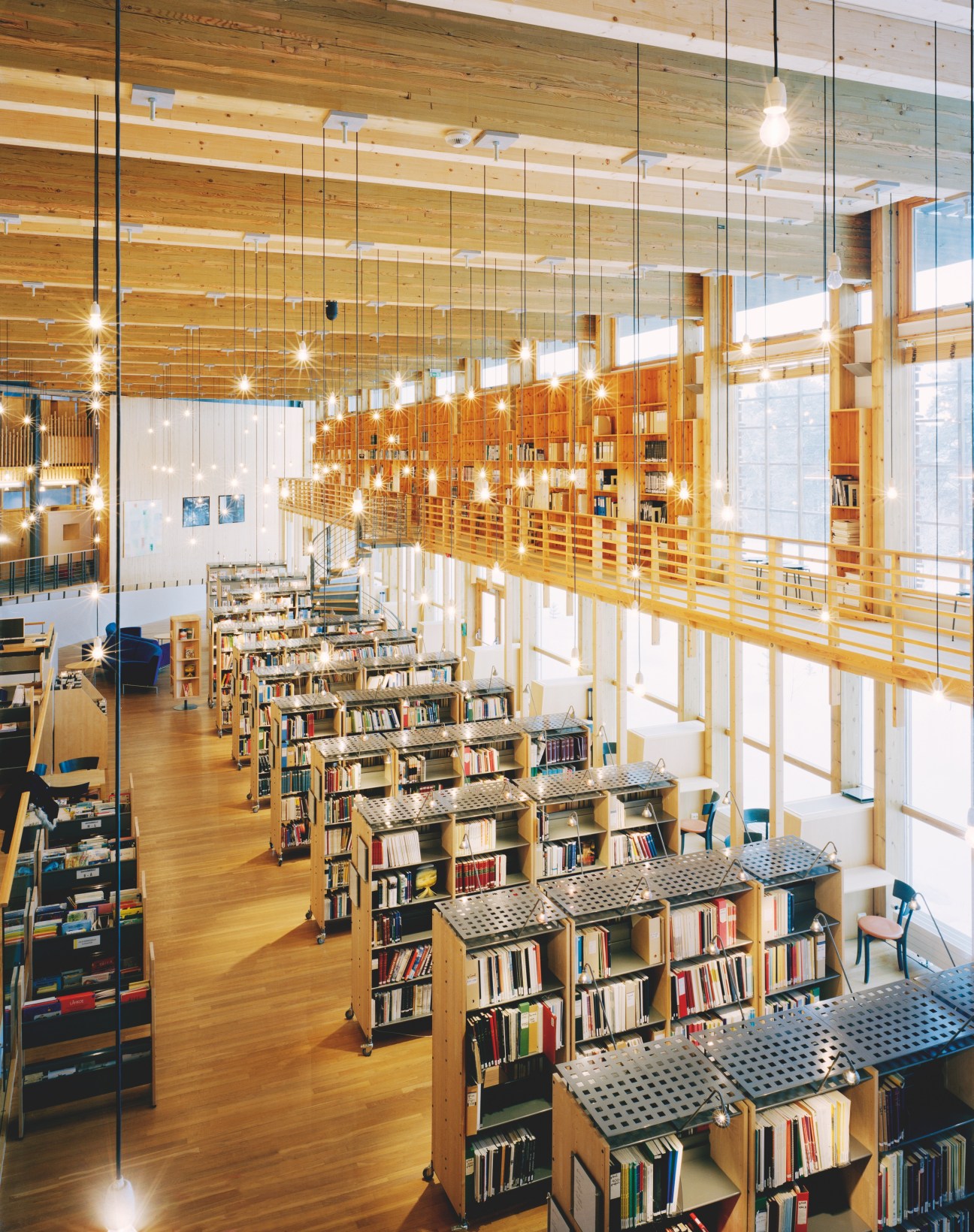 Modern library interior with wooden bookshelves, glass partitions, and pendant lights in the Norwegian Sámi parliament building.