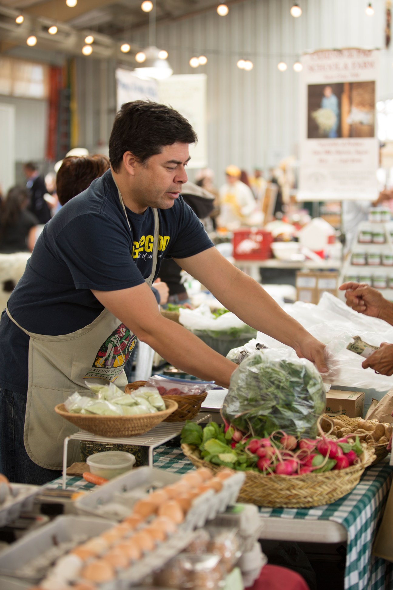 A vendor arranges fresh produce at Santa Fe Farmers Market, with radishes and leafy greens displayed in baskets.