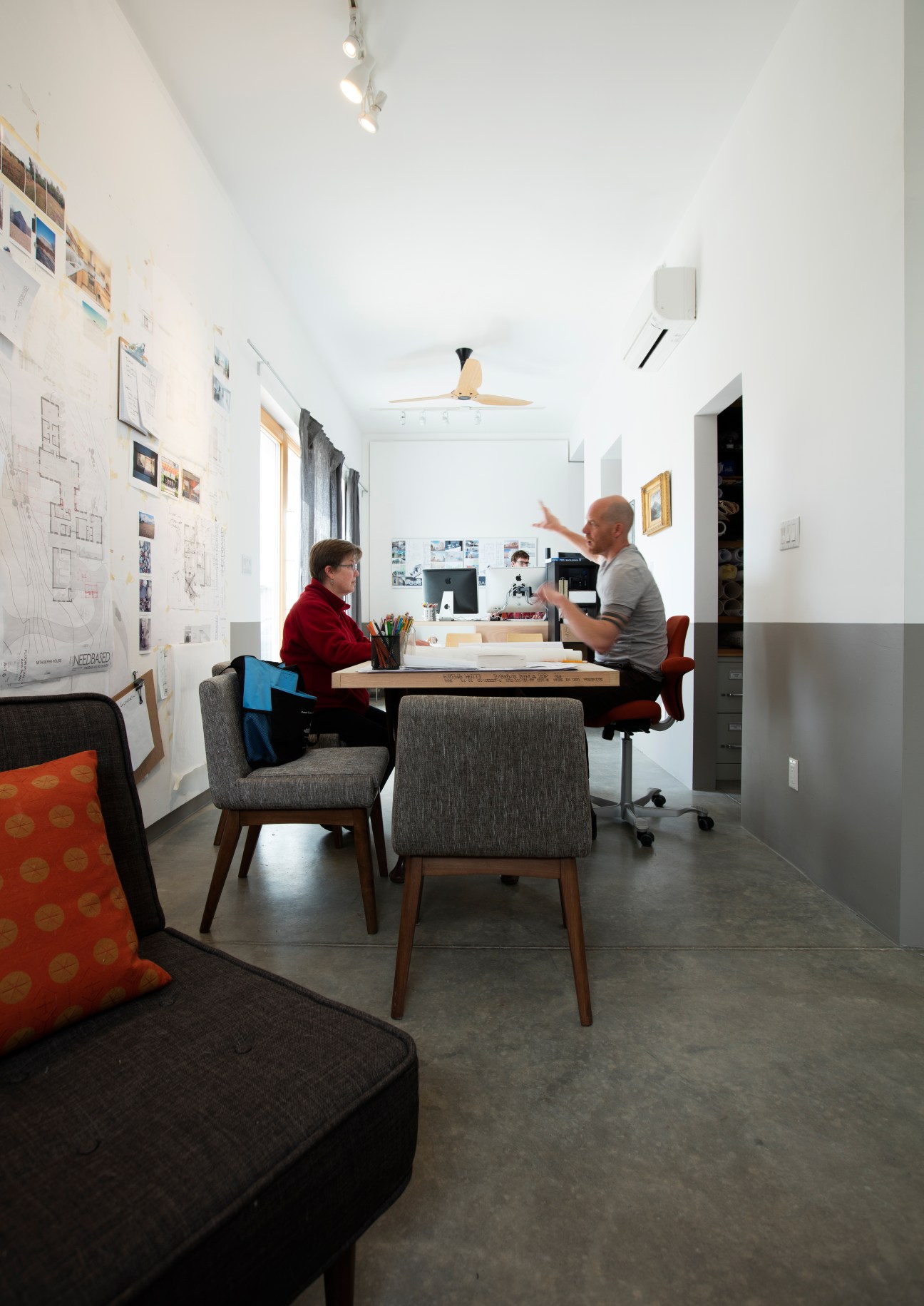 Jonah Stanford discusses architectural plans with a client in a bright, modern home studio with design sketches on the walls.