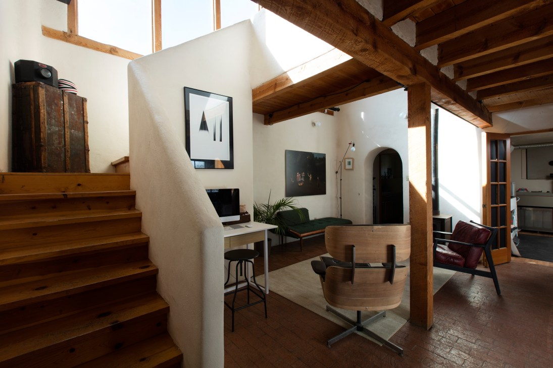 Light-filled home studio with wooden beams, white walls, desk workspace, and modern furnishings.