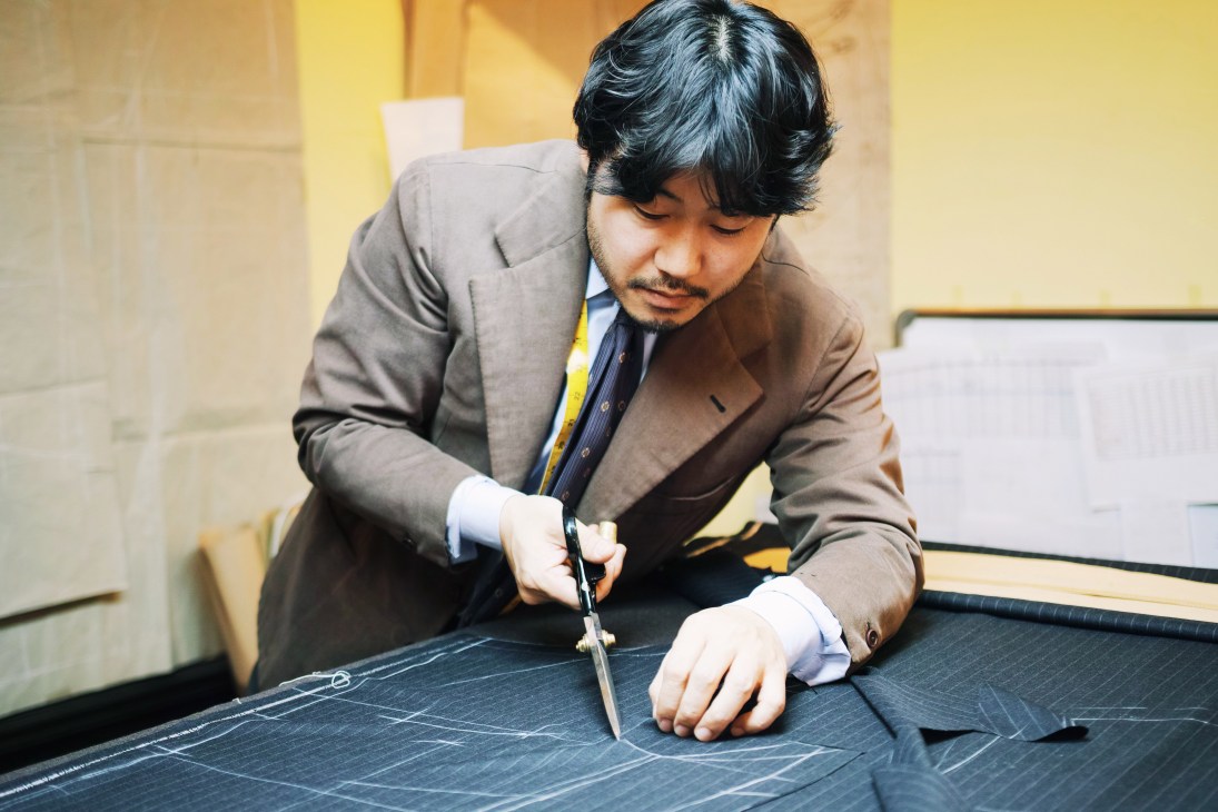 Man in tailored suit cutting fabric pattern at a work table