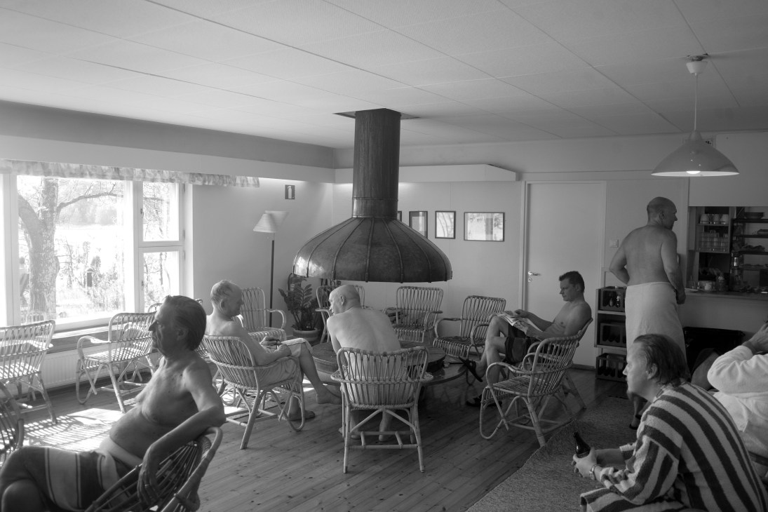Members relax in chairs around a central wood-burning sauna stove at the Finnish Sauna Society in Helsinki.