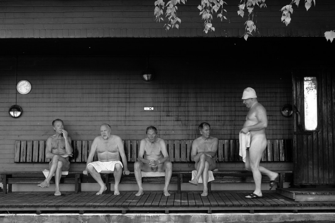 Men relaxing on wooden bench inside Finnish Sauna Society sauna facility.
