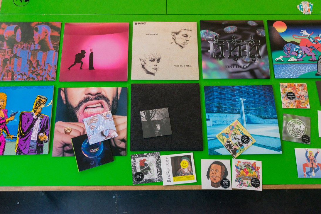 Colorful vinyl records and album covers from the Bromance record label displayed on a bright green wall.