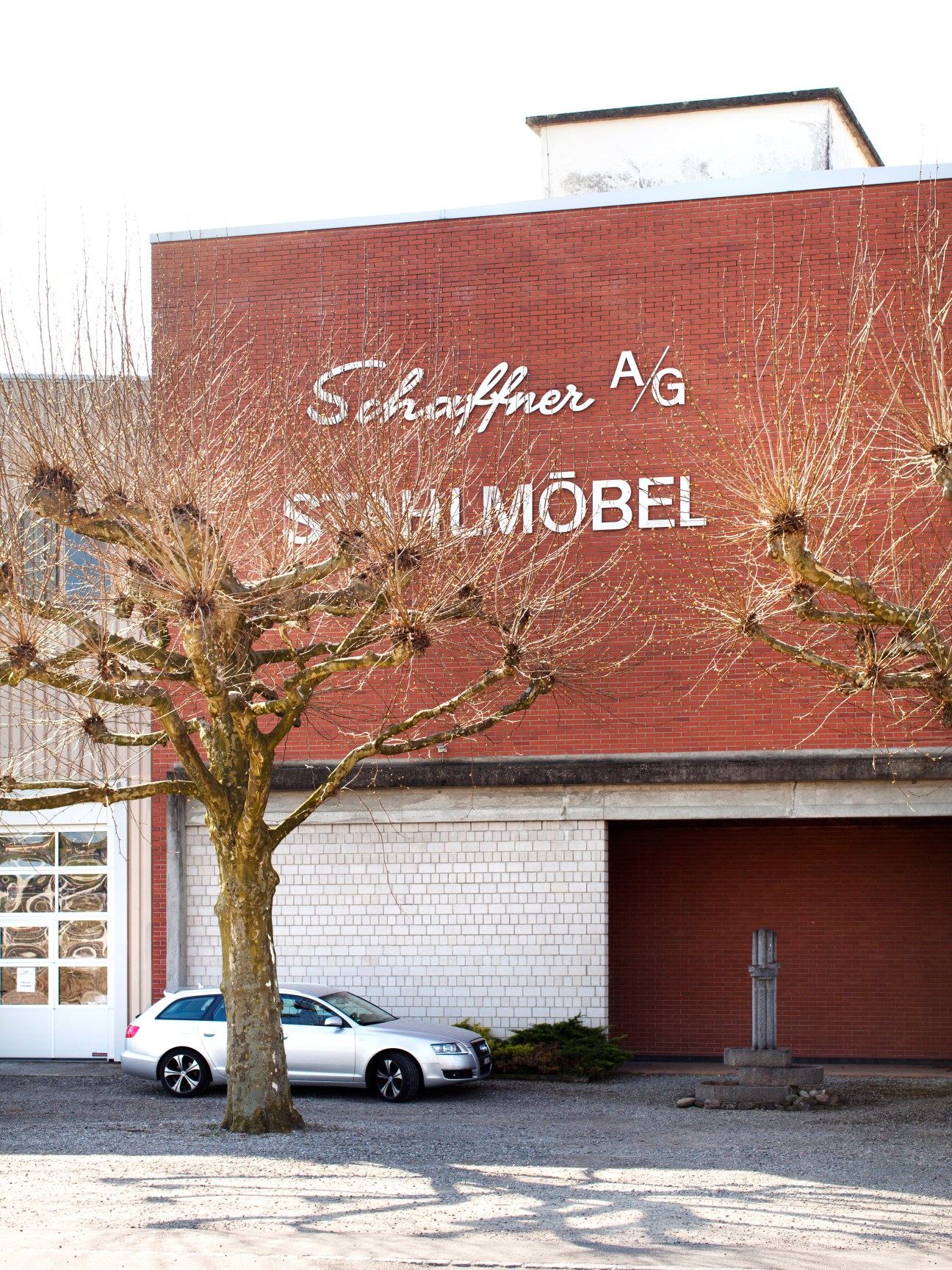Red brick factory building with Schaffner AG signage, bare tree, and parked car in front