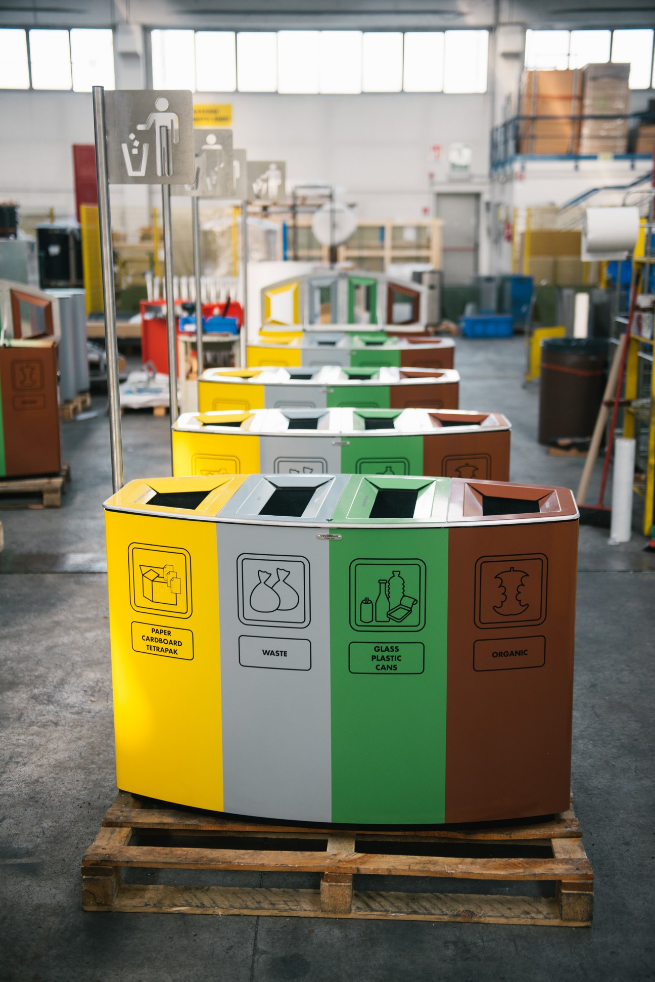 Colorful multi-section recycling bin with yellow, grey, green and brown compartments labeled for different waste types in Metalco workshop.