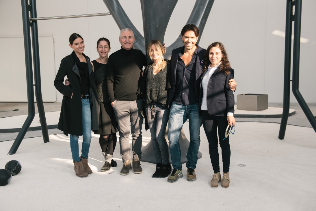 Six people posing together in front of large curved metal structures in a bright showroom space.