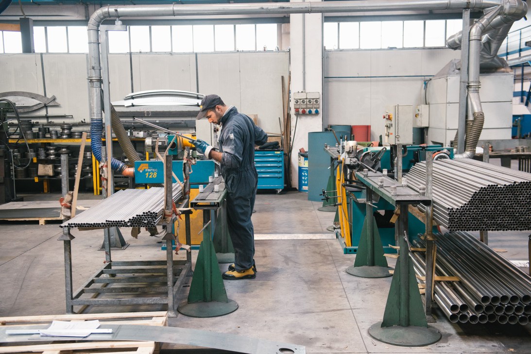 Worker in dark clothing assembles metal pipes in Metalco's manufacturing workshop with industrial machinery.