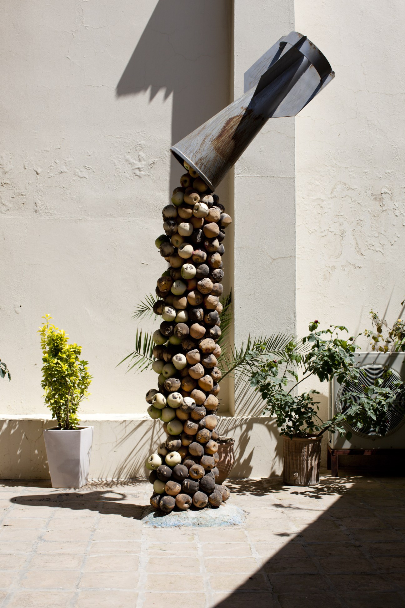 Sculpture of a chemical bomb depicting shells stacked beneath an inverted metal container on white wall.