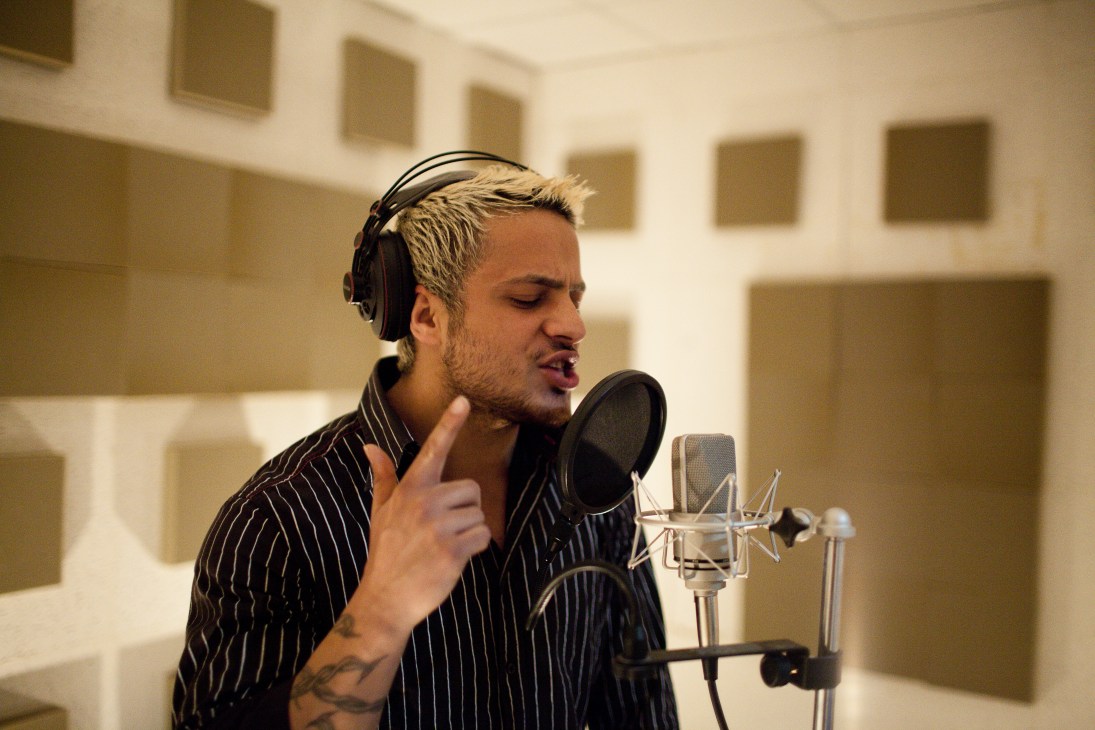 Rapper Serhang Mohammad recording in a studio, wearing headphones and a pinstriped shirt.